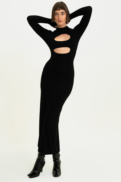 Model in Peek-A-Boo Black Dress with hands raised, showcasing long sleeves, thumbholes, and elegant cut-out details.